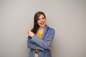 Smiling woman in blue business suit pointing finger at side, isolated female portrait.