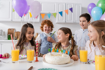 group of happy children celebrating birthday next to tasty cake during party at home.