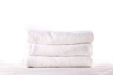 Stack of neatly folded towels on a rustic wooden table, waiting to be used. Showcase of a cozy bathroom or spa setting against a plain white background. Studio shot, close up, copy space.