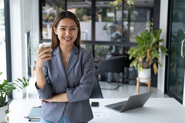 Wall Mural - Young pretty businesswoman having a coffee break, smiling and holding a coffee cup in the office room.