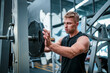 © FotoArtist - Male athlete exercising in the gym, lifting weights, pulling joints.