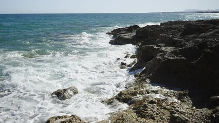 Wall Mural - Rocks in the sea of Spain at a strong wind. White splashing waves crash against the shore. sunny spring day