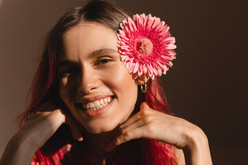 Wall Mural - Close up stylish trendy-looking young woman appearance wearing her bright pink hair smiling broadly, demonstrating her perfect white teeth. Happiness woman wear pink top and gerbera flower in hair.