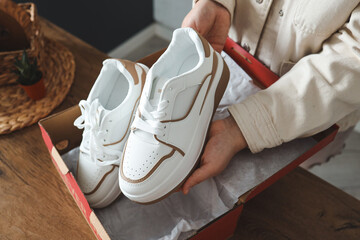 Wall Mural - Unpacking women's shoes, stylish white sneakers in hands