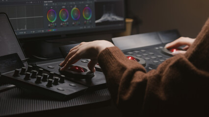 Fototapete - Female editor works in studio, uses digital color grading control panel. Colorist makes video color correction on computer. Program interface with RGB graphics, color wheels and levels on PC monitor.
