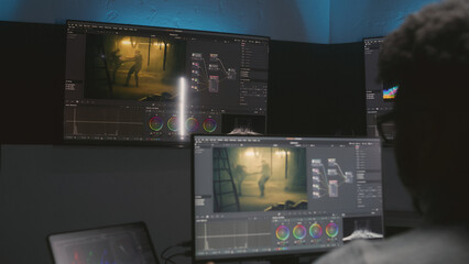 Fototapete - African American movie maker does color grading on computer in studio with equipment. Big monitors with action film footage and professional software interface on wall. Video post production process.