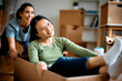 © Drazen - Happy Asian woman has fun while being pushed by her female friend in cardboard box after moving into new apartment.