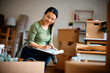 © Drazen - Happy Asian woman going through list of her belongings on moving day.