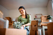 © Drazen - Happy Asian woman packing her plants while relocating into new apartment.