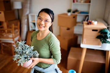 Wall Mural - Happy Asian woman with flower pot at her new apartment looking at camera.