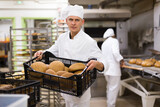 Fototapeta Do przedpokoju - Portrait of focused male chef standing in bakery kitchen with fresh bread in crate