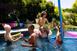 Happy diverse group of friends having pool party, playing in swimming pool in garden
