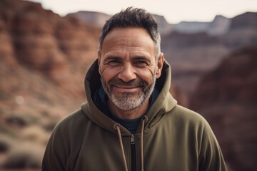 Wall Mural - Medium shot portrait photography of a grinning man in his 40s wearing a stylish hoodie against a canyon or desert landscape background. Generative AI