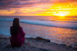 Girl in pink tracksuit sits on magnificent Ten Mile beach and enjoys colorful sunrise over Pacific ocean. Black rocks campground, NSW, Australia