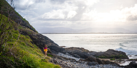 Beautiful girl stand on large rocks and admires powerful  waves in popular Byron Bay, NSW, Australia