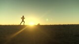 Fototapeta Kosmos - running after sun. training jogging. A healthy beautiful girl is engaged in fitness, jogging in country in sun. Jogger girl breathes fresh air on field. Free young woman runs in summer park at sunset.