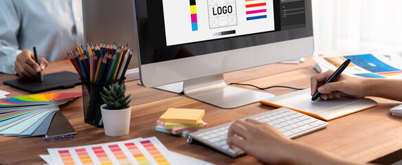 Poster - Graphic designer work on computer laptop and with graphic drawing pen while brainstorming unique design with professional graphic team in modern digital studio workplace. Panorama shot. Scrutinize