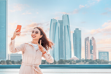 Wall Mural - Embodying the spirit of modernity and progress in the UAE's capital city, a girl snaps a selfie against the dazzling skyline of Abu Dhabi.