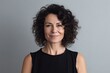 © pixardi - Smiling brunette woman, mid-aged, curly hair, arms crossed, grey background. Photo generative AI