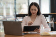 © Songsak C - An Asian businesswoman using a digital tablet while sitting at a work desk in an office