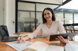 © Songsak C - Portrait of Asian businesswoman with laptop writes on a document at her desk in a cafe.