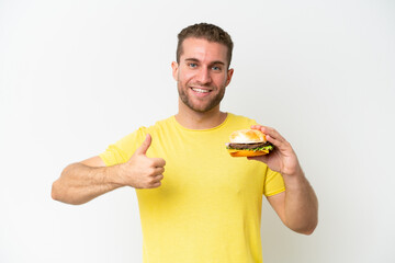 Canvas Print - Young caucasian man holding a burger isolated on white background with thumbs up because something good has happened