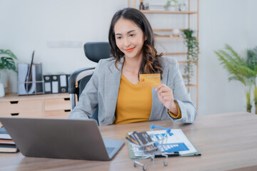 Businesswoman hand holding credit card and use laptop and chart information on work table in office.