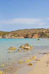 Canvas Print - Vertical shot of rocks on the sea near the beach and a cliff in the background under blue sky