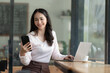 © Songsak C - A happy young Asian woman talking on her mobile phone and smiling while sitting at her working place in a cafe.
