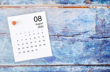 the august 2023 monthly calendar and wooden push pin on blue wooden background.
