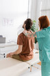 redhead osteopath touching painful back of man sitting on massage table in consulting room.