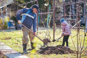 Happy father and daughter planting a new tree in the village in spring