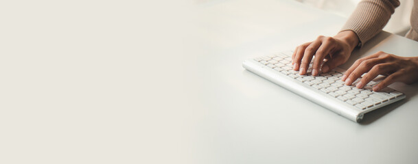 Wall Mural - Cropped shot of young woman typing on keyboard computer on white table with copy space.