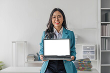 Happy Asian Business Woman Holding Laptop With Blank Screen Stands In A Modern Office Looking At The Camera And Smiling Friendly