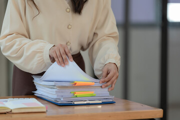 businesswoman hands working in stacks of paper files for searching and checking unfinished documents