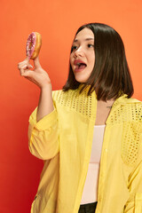 dessert lover. portrait of young, pretty, asian girl in yellow blouse, holding pink donut, posing ag