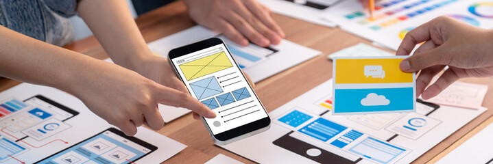 Panorama shot of front-end developer team brainstorming UI and UX designs for mobile app on paper wireframe interface. User interface development team planning for user-friendly UI design. Scrutinize