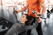 Attractive young woman working out with dumbbells in gym, male muscular trainer helping her. Close up.