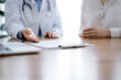 © rogerphoto - Doctor and patient discussing something while sitting near each other at the wooden desk in clinic. Medicine concept