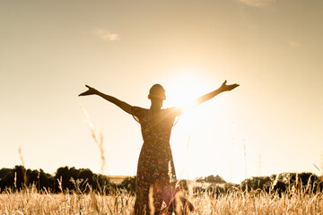 Joyful young woman with arms up to the sunlight feeling happy and free in nature 