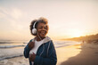 Happy mature woman listening music jogging on sea shore, generative ai