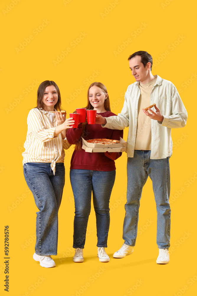 Happy friends with tasty pizza and drinks on yellow background