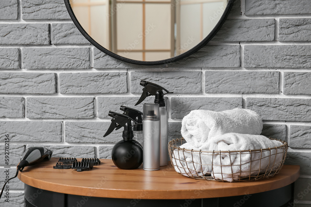 Different sprays, towels and hair clipper on table near grey brick wall