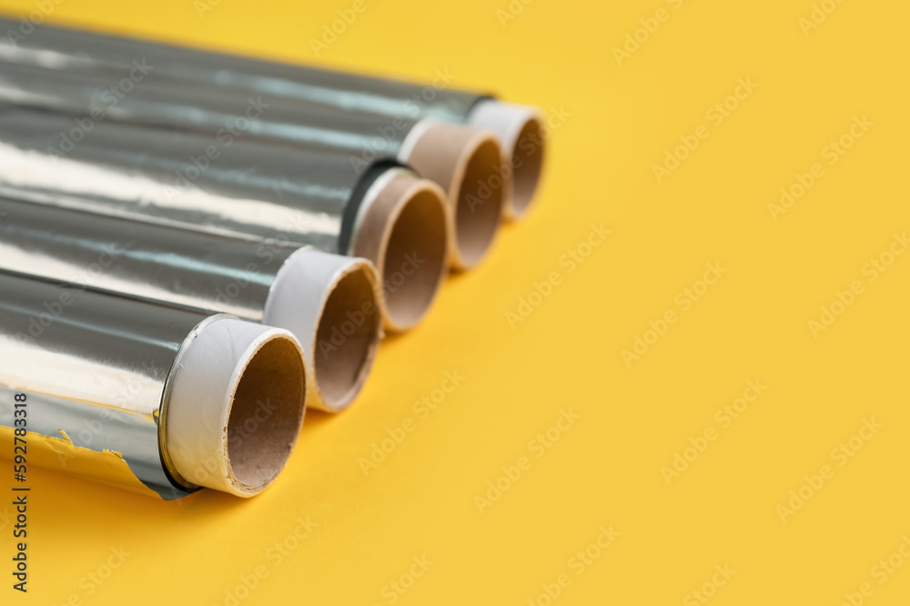 Aluminium foil rolls on yellow background, closeup