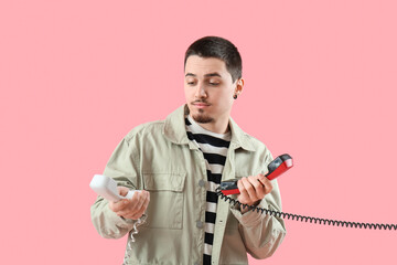 Handsome young man with two phone receivers on pink background