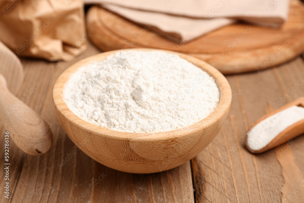 Bowl with wheat flour on wooden table, closeup
