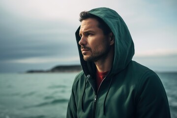 Portrait of a handsome young man in a green hooded jacket on the seashore.