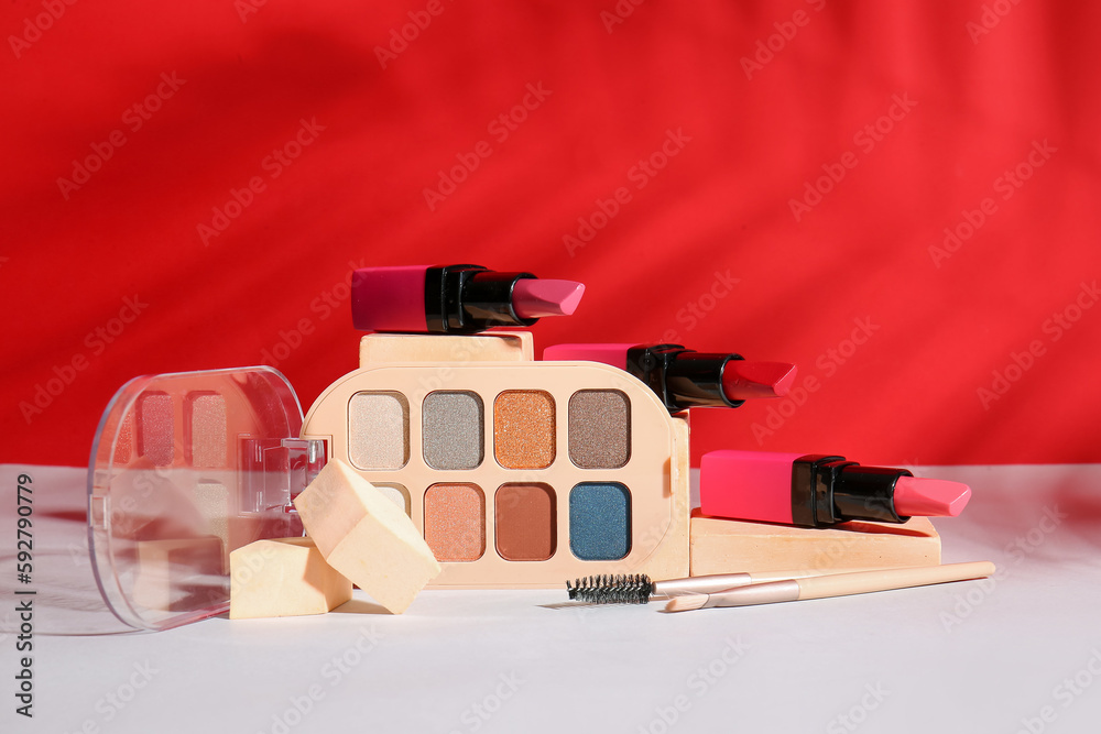 Decorative cosmetics with makeup brushes and sponges on table near red wall