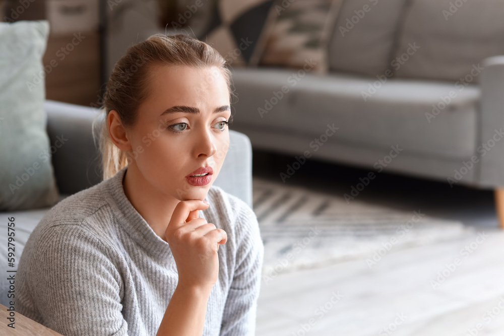 Thoughtful young woman sitting on floor at home, closeup