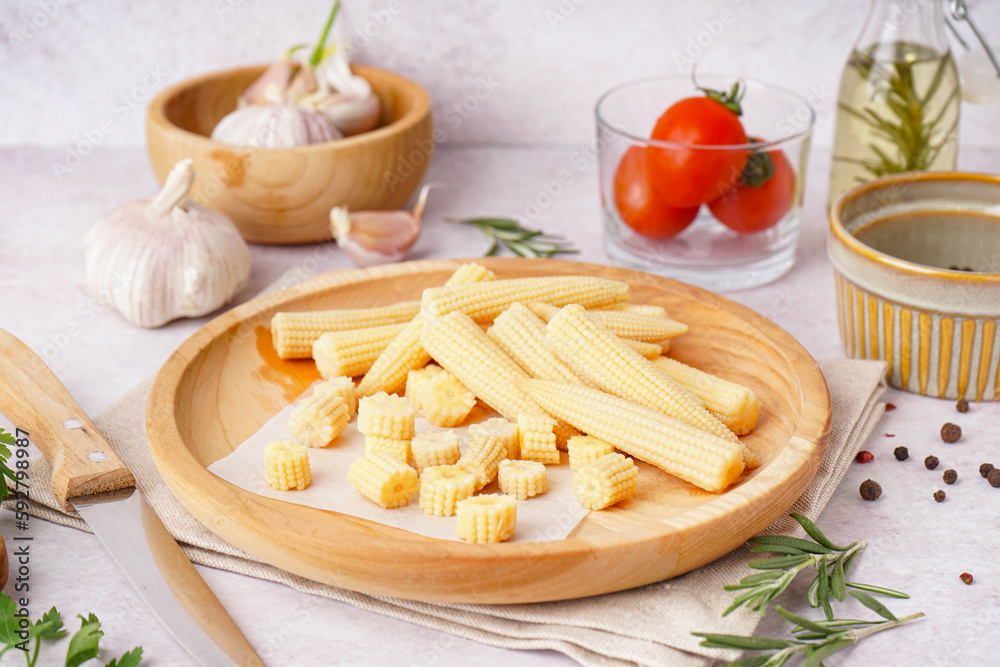 Plate with cut and whole canned baby corn cobs on light background